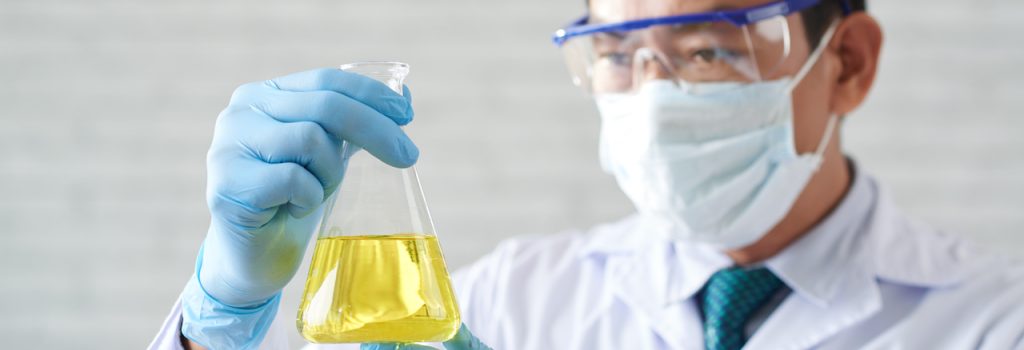 Researcher looking a beaker with yellow liquid in his hands